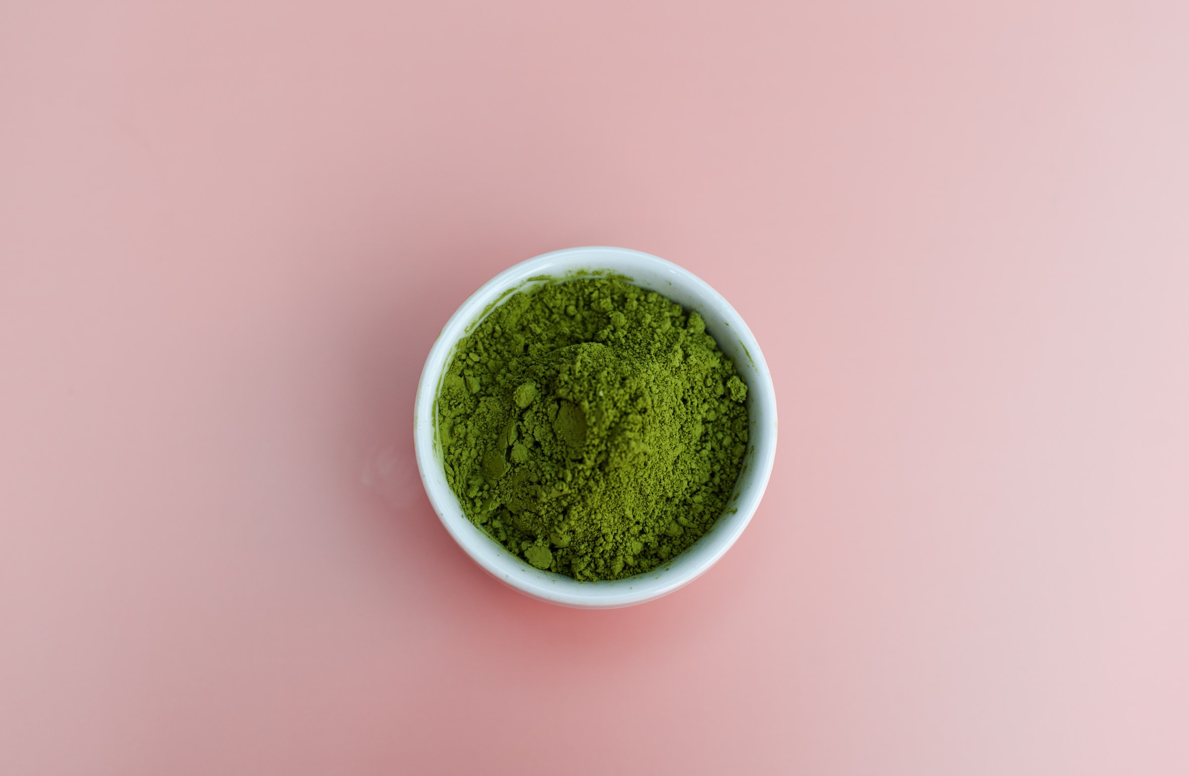 A bowl with kale powder on a pink background